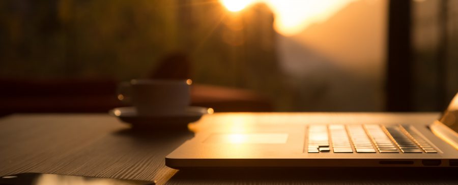 Computer Coffee Mug and Telephone on black wood table sun rising
